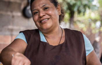 Vertical photo of a smiley woman in apron frying food in a community outdoor rural kitchen